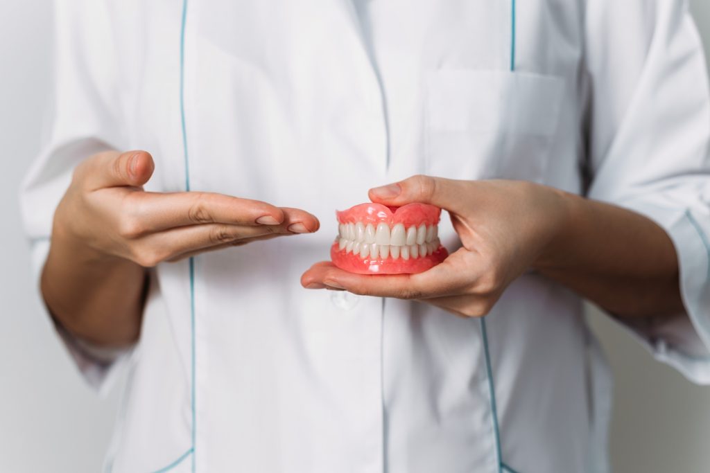 The dentist is holding dentures in his hands. Dental prosthesis in the hands of the doctor close-up