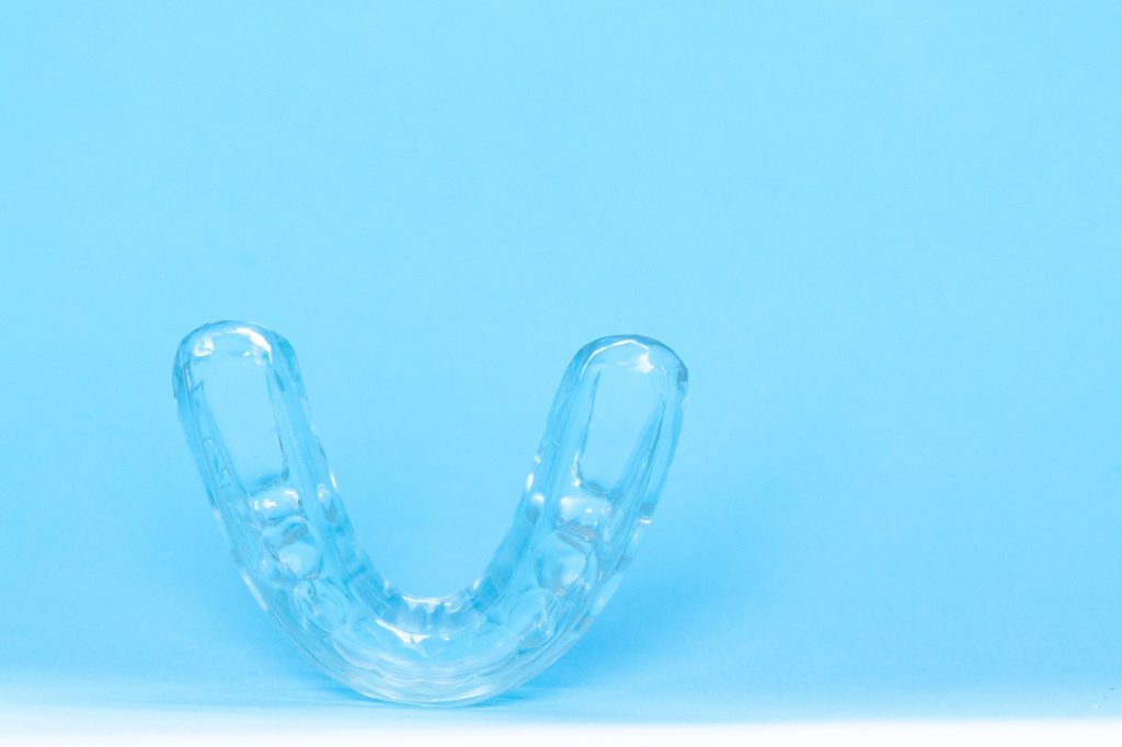 Silicone dental mouthguard, orthodontic trainer to correct bite on blue background,
